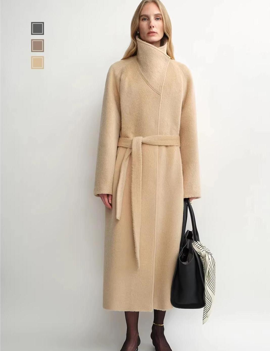 Woman wearing a beige coat with a belt, holding a black handbag on a white background.