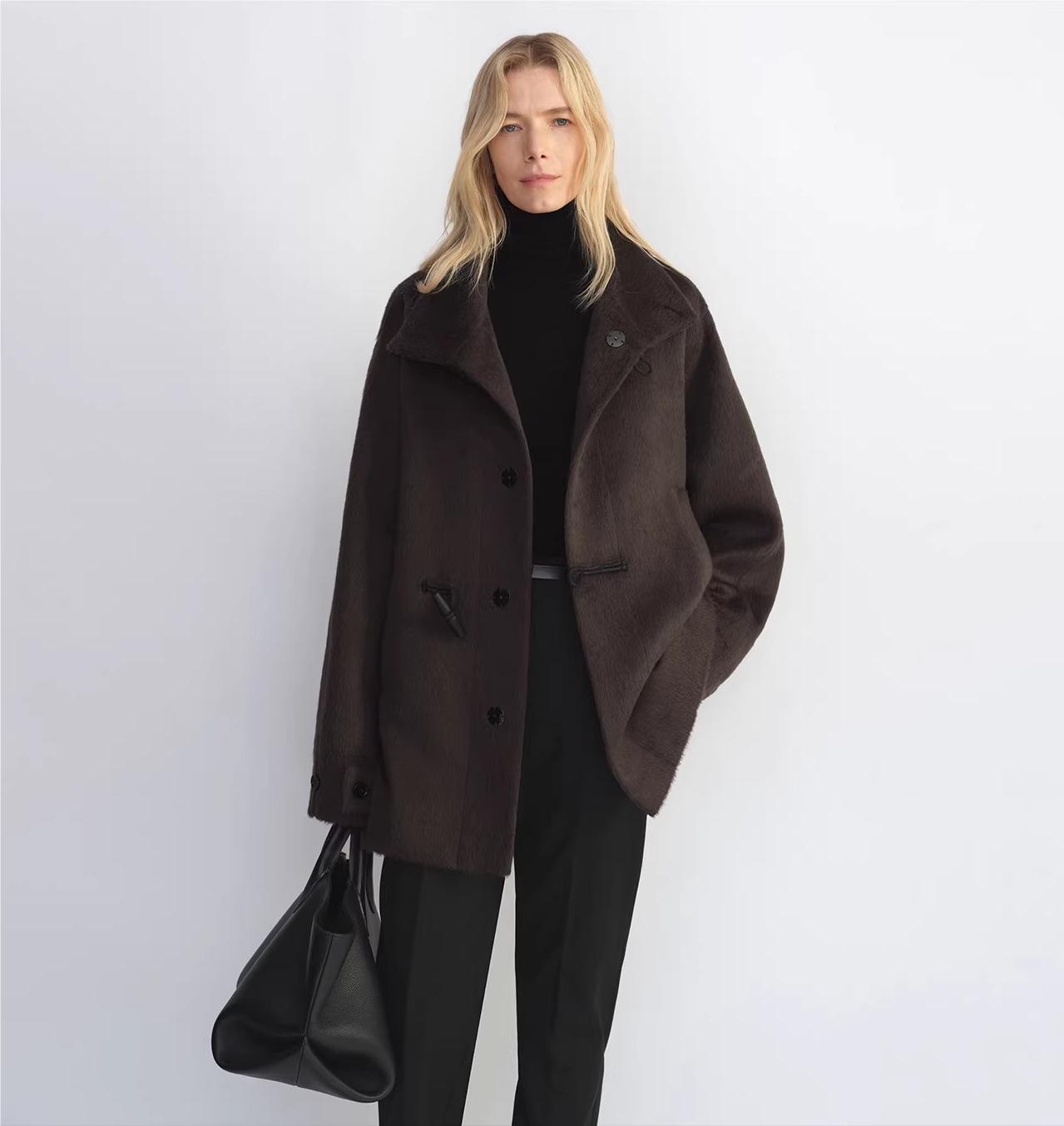 Woman wearing a brown coat holding a black handbag against a white background