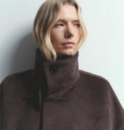 Person wearing a brown coat with a high collar against a plain background